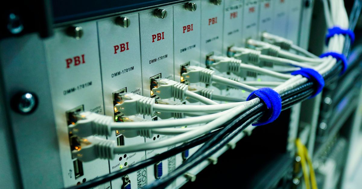 Weiße Netzwerkkabel werden mit blauen Kabelbindern zu einem Bündel zusammengefasst und an einem Serverrack befestigt.