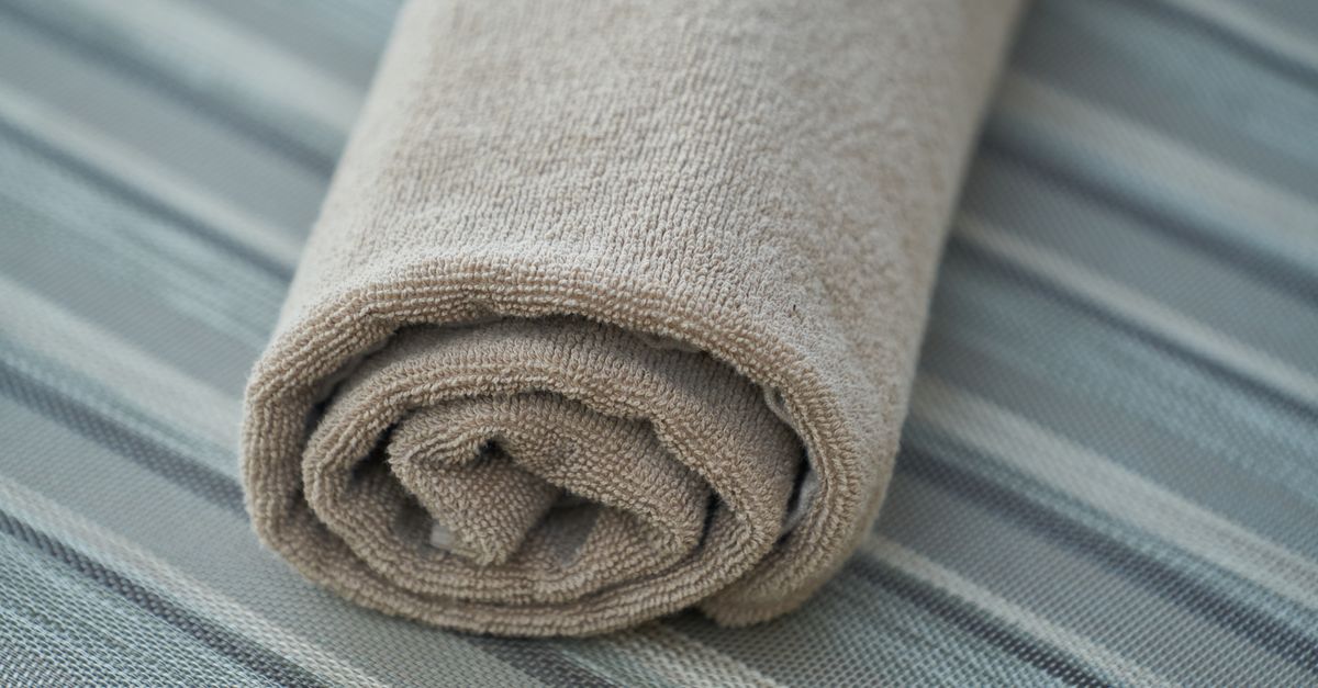 Ein zusammengerolltes, flauschiges Frottee-Handtuch in Beige mit sichtbarer Schlingenstruktur.