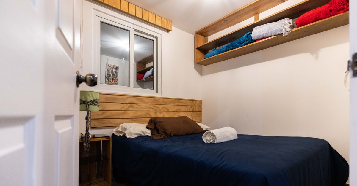 Rot und blau gefaltete Handtücher liegen ordentlich gestapelt auf einem Holzregal über einem Bett mit dunkelblauer Bettwäsche.