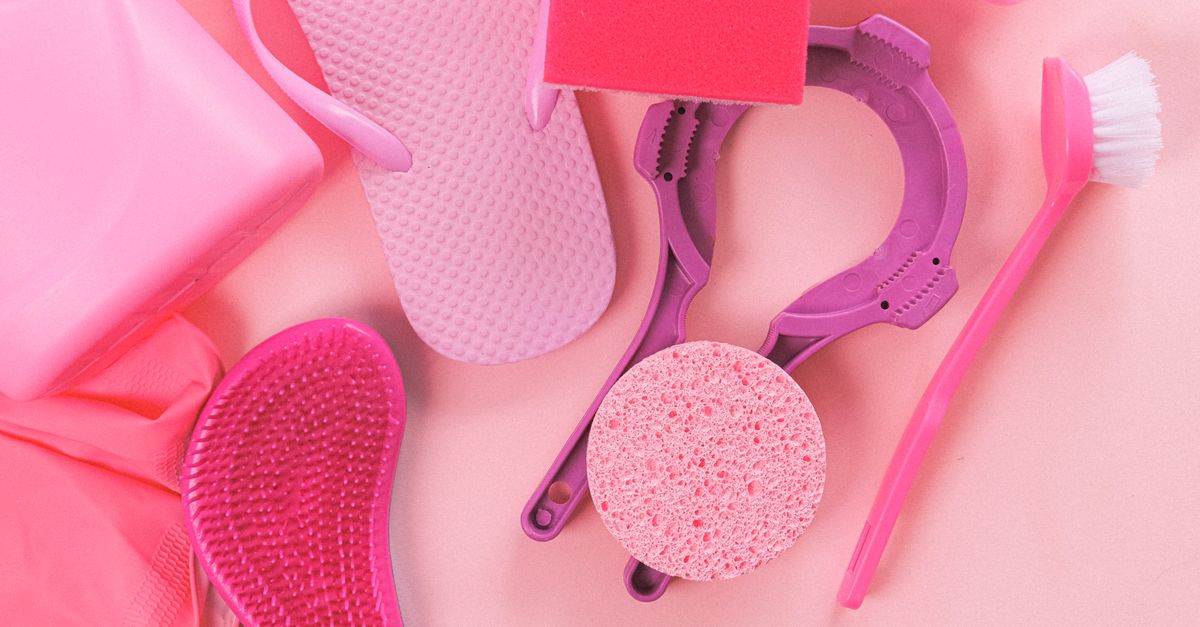 Verschiedene rosa Reinigungsutensilien wie Schwamm, Bürste und Handschuh liegen auf einer rosa Oberfläche.