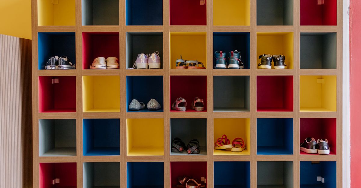 Ein buntes Würfelregal in Rot, Gelb, Blau und Grau mit ordentlich einsortierten Kinderschuhen in einzelnen Fächern.