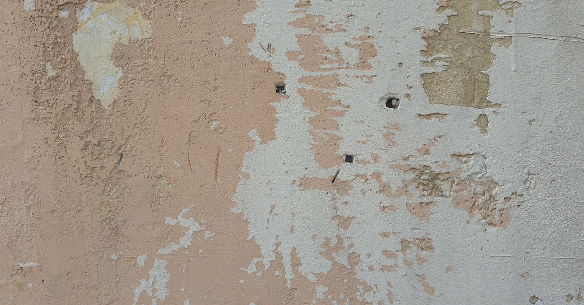 Verwitterte Wand mit abblätternder Farbe und mehreren kleinen Bohrlöchern.