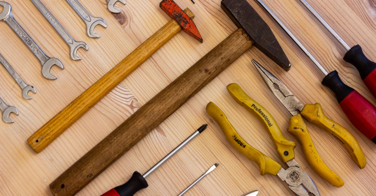 Verschiedene Werkzeuge wie Schraubenschlüssel, Hammer, Schraubendreher und eine Zange liegen auf einem Holzbrett.