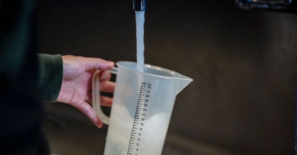Eine Hand hält einen Messbecher unter einen laufenden Wasserhahn, während Wasser hineinfließt.