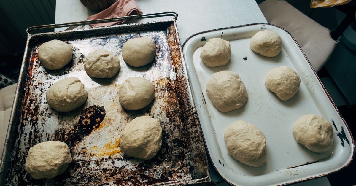 Zwei Backbleche mit mehreren runden Portionen Brotteig, die zum Gehen bereitstehen.