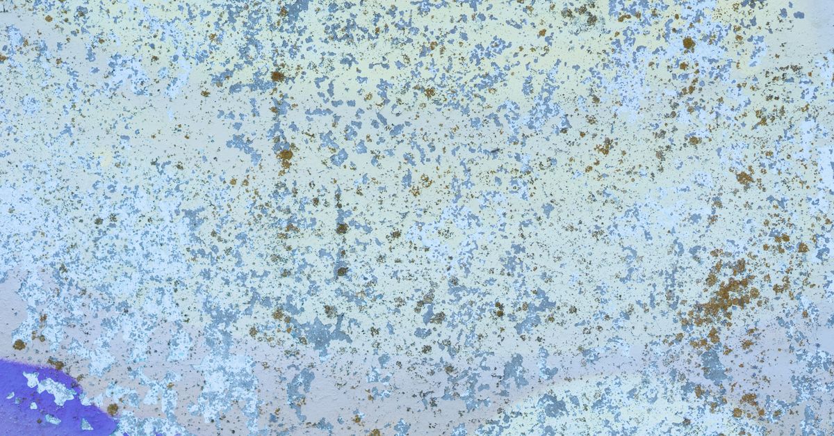 Verwitterte Wand mit abblätternder Farbe und rostfarbenen sowie bläulichen Flecken, die eine fleckige, verblasste Textur zeigen.