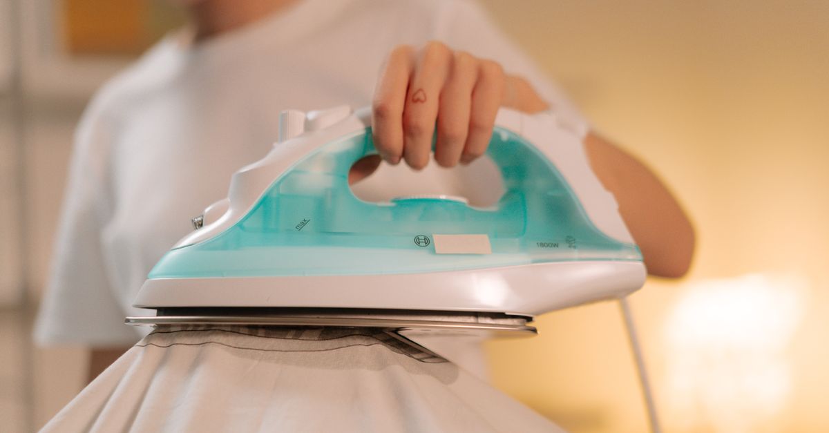 Nahaufnahme eines Dampfbügeleisens mit durchsichtigem Wassertank, das über einen hellen Stoff geführt wird.