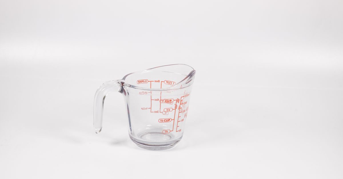 Ein durchsichtiger Messbecher aus Glas mit roten Maßeinheiten für Cups und Milliliter steht vor weißem Hintergrund.