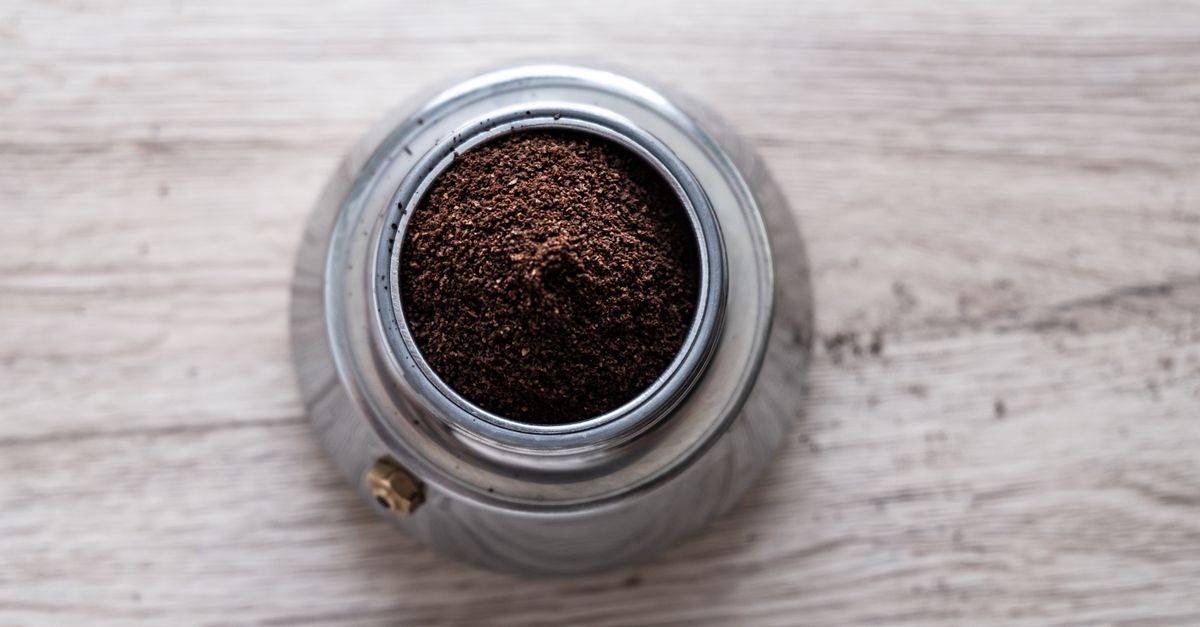 Gemahlener Kaffee gefüllt in den Siebträger einer Espressokanne, von oben fotografiert auf einer Holzoberfläche.