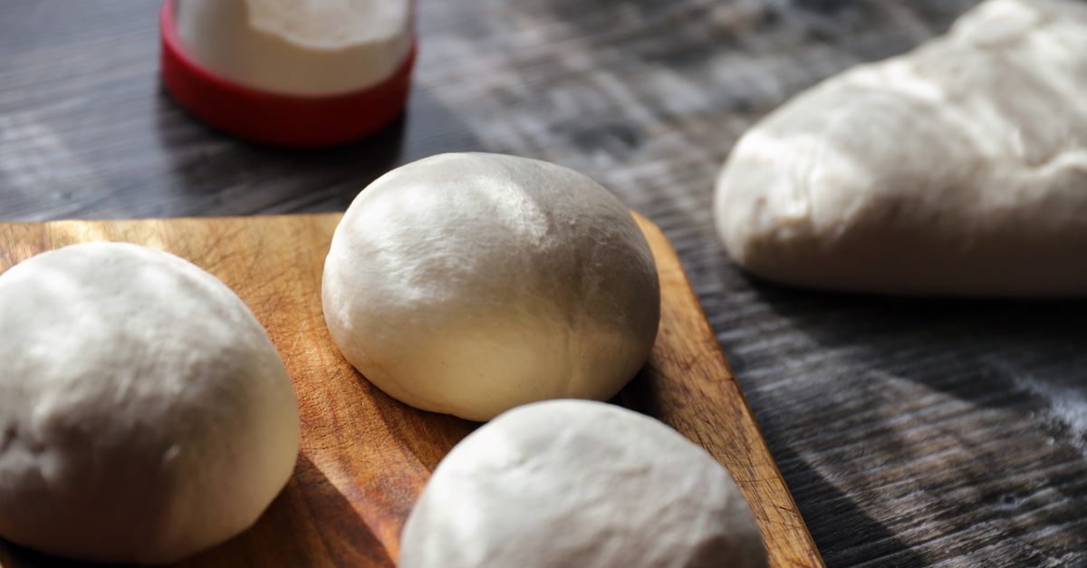 Mehrere rohe, runde Teigknödel liegen auf einem Holzbrett, bereit zum Kochen.