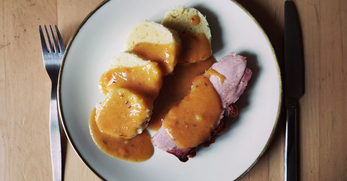 Geschnittene Semmelknödel mit Bratensoße und Fleisch auf einem weißen Teller.