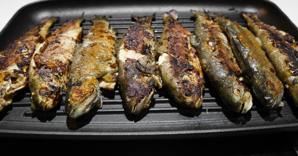 Mehrere ganze Fische liegen in einer schwarzen Grillpfanne mit gebräunter, knuspriger Haut.
