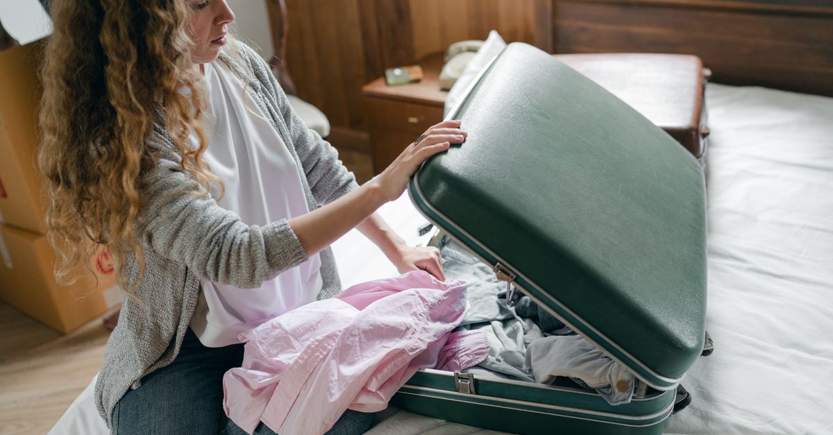 Eine Frau packt Wäsche in einen grünen Koffer, der auf einem Bett liegt.