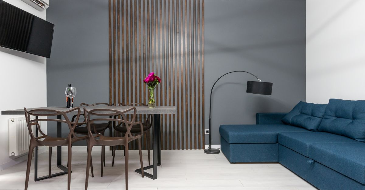 Modernes Wohnzimmer mit vertikaler Holzlamellen-Wandverkleidung als Akustikelement hinter einem Esstisch und einem blauen Sofa.