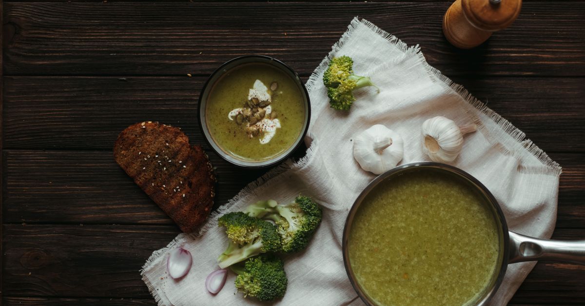 Aufgewärmte Brokkolisuppe in einem Topf und einer Schale, daneben Brot, Knoblauch und Brokkoliröschen.
