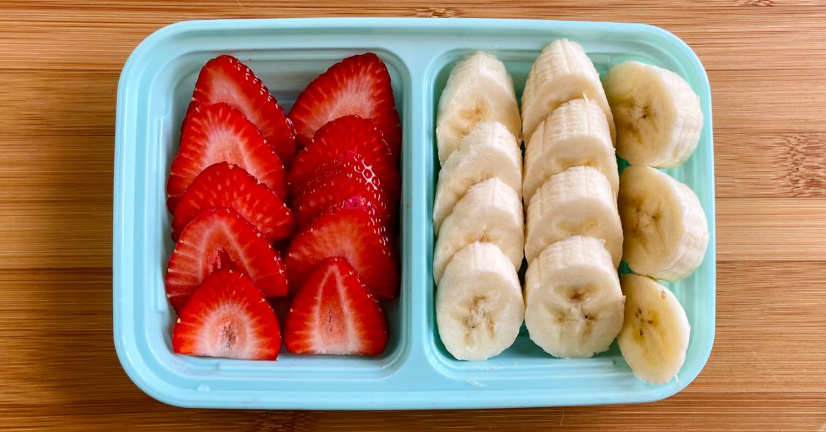 Eine hellblaue, unterteilte Aufbewahrungsbox von oben, gefüllt mit geschnittenen Erdbeeren und Bananenscheiben.