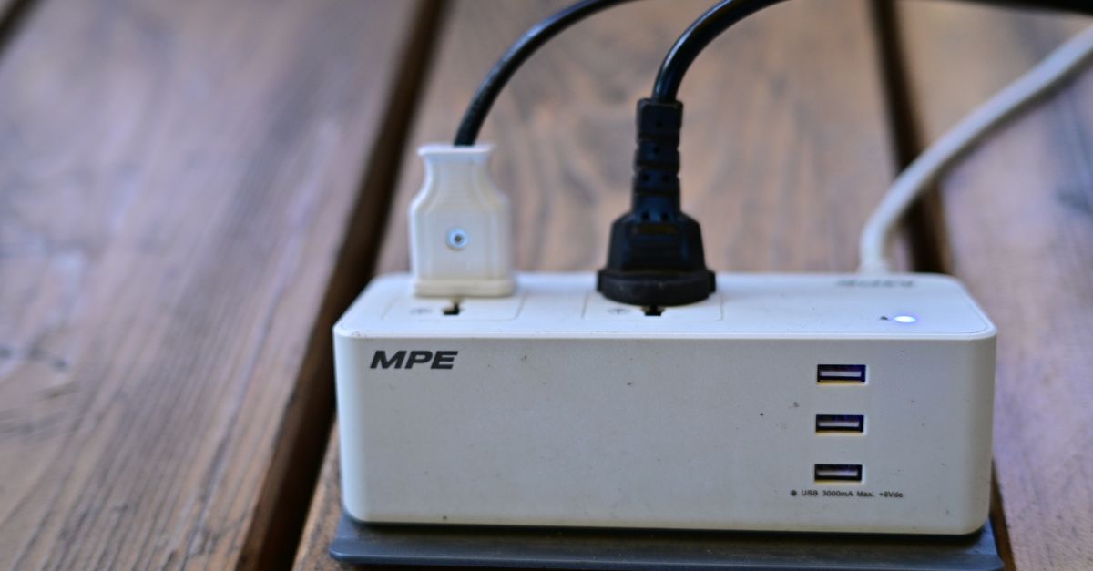Eine weiße Steckdosenleiste mit mehreren angeschlossenen Geräten und USB-Anschlüssen auf einem Holztisch.