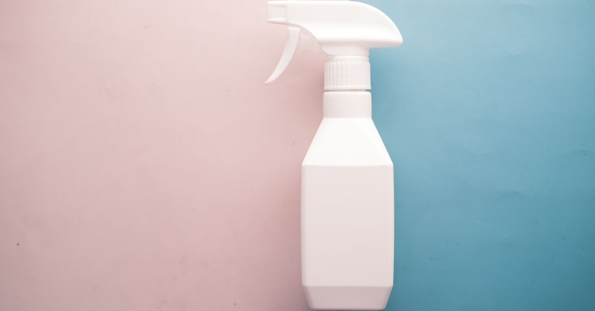 Eine weiße Sprühflasche steht vor einem rosa-blauen Hintergrund.