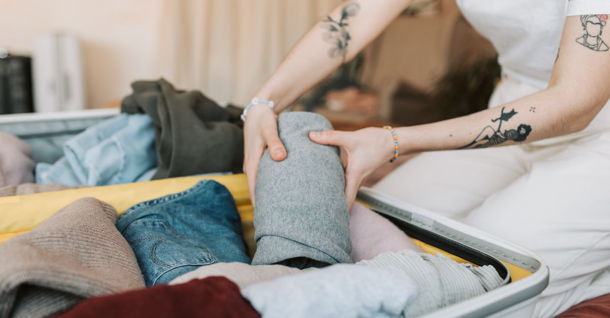 Eine Person rollt Kleidungsstücke zusammen und packt sie in einen offenen Koffer.
