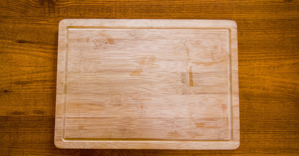 Ein sauberes, leeres Holzschneidebrett liegt auf einem dunklen Holztisch.