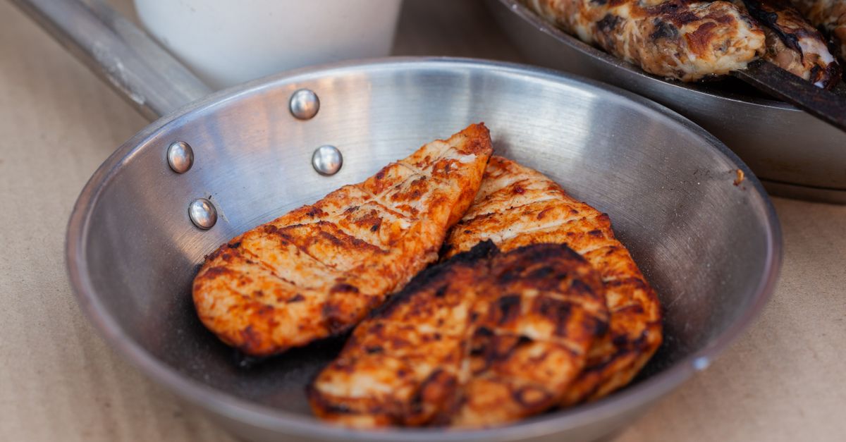 Zwei gebratene Hähnchenbrustfilets mit goldbrauner Kruste liegen in einer Edelstahlpfanne.