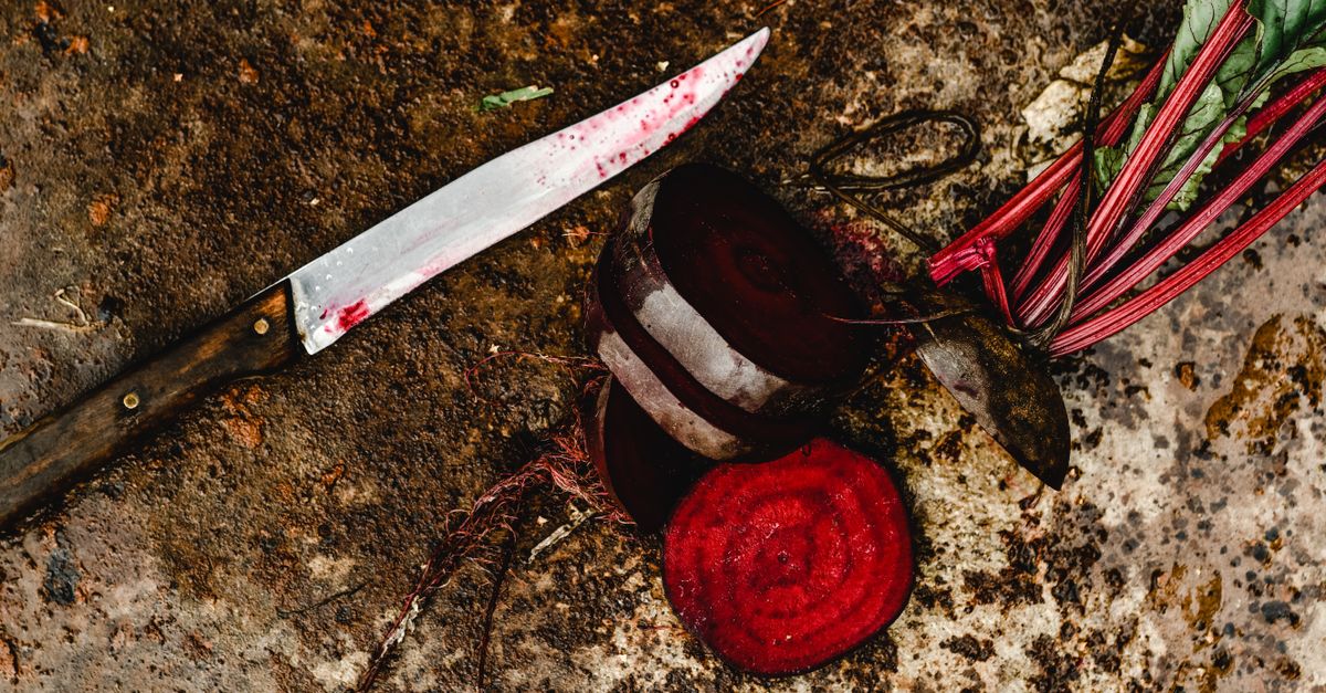 Ein Messer mit roten Saftspuren liegt neben aufgeschnittener roter Bete auf einer fleckigen Steinfläche.