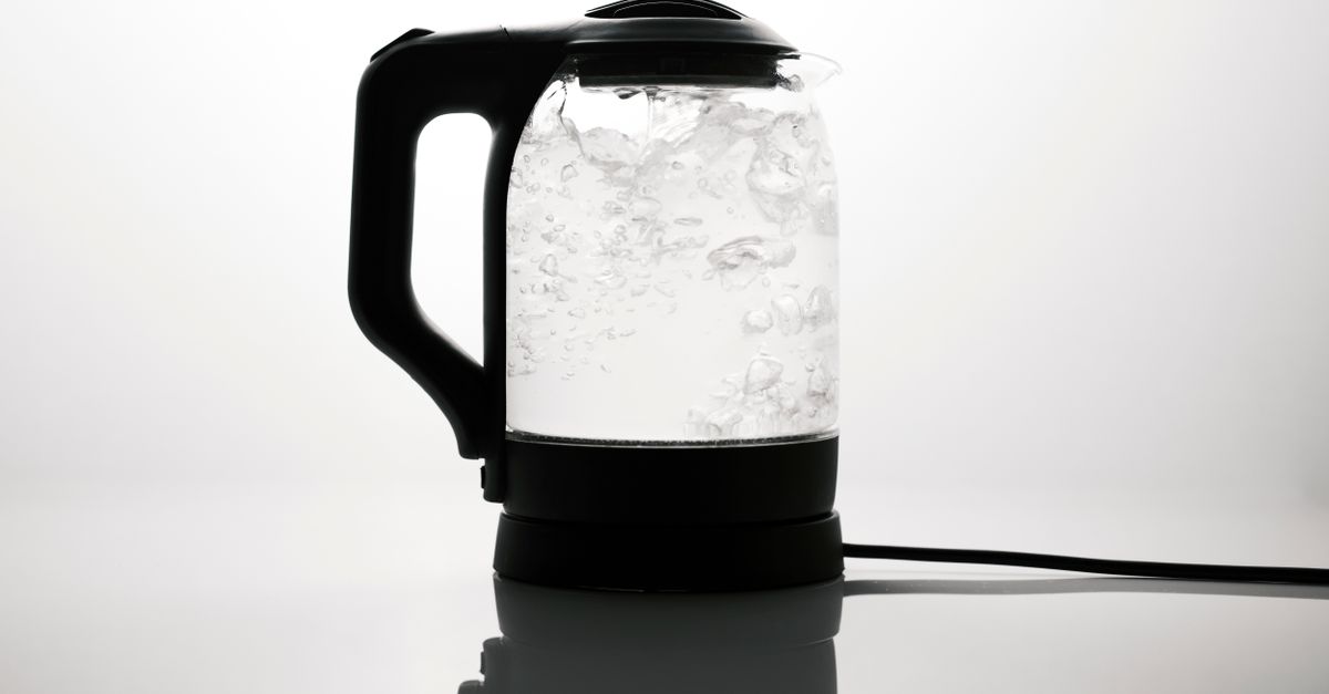 Ein moderner Glaswasserkocher mit klarem, kochendem Wasser auf schwarzem Sockel vor hellem Hintergrund.