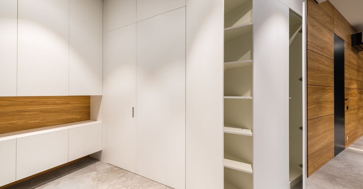 Ein schmaler Einbauschrank mit offenen weißen Regalfächern neben einer Holztür im Flur eines modernen Hauses.