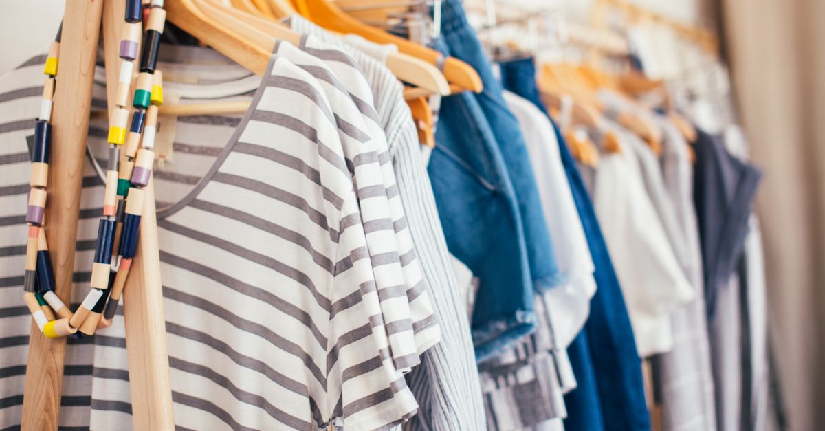 Ordentlich aufgehängte Kleidungsstücke wie gestreifte Shirts und Jeans an Holzbügeln in einem offenen Kleiderschrank.