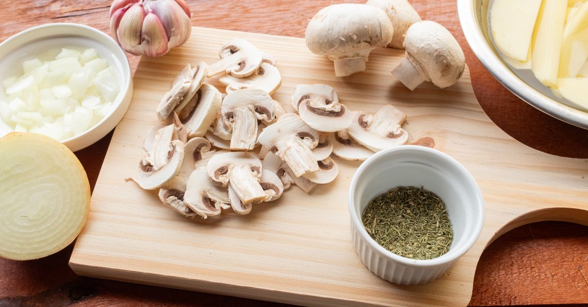 Gehackte Zwiebelwürfel liegen in einer weißen Schale neben einer halben Zwiebel auf einem Holzschneidebrett.