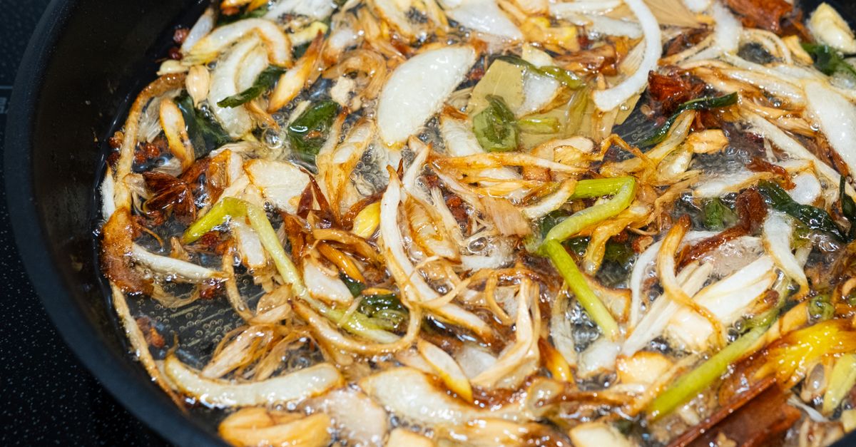 Zwiebelstreifen brutzeln goldbraun und knusprig in heißem Öl in einer Pfanne.