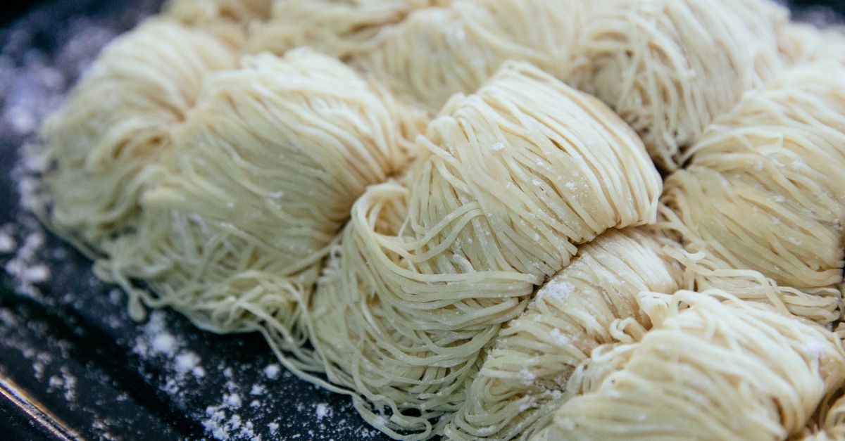 Frische, mit Mehl bestäubte Nudelnester liegen portionsweise auf einem dunklen Blech.