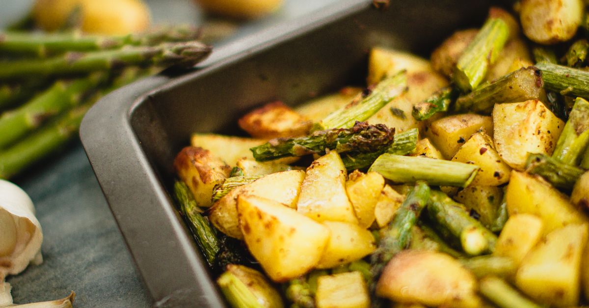 Nahaufnahme einer Auflaufform mit gerösteten Kartoffelwürfeln und grünem Spargel mit karamellisierten Rändern.