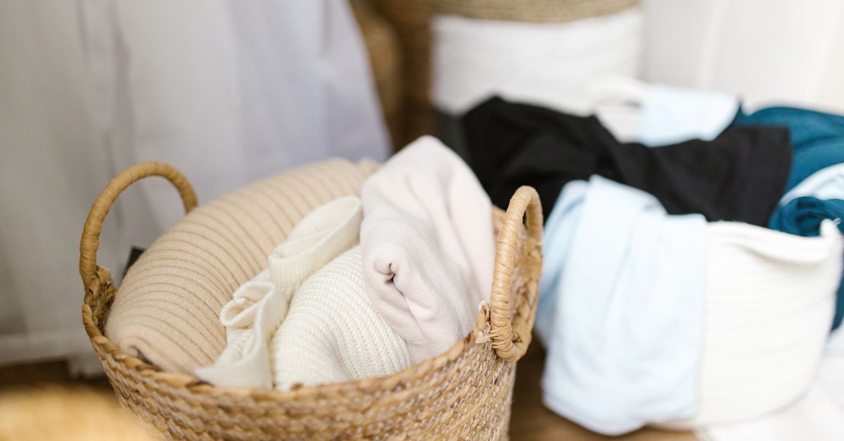 Ein geflochtener Wäschekorb mit gefalteter, cremefarbener Kleidung steht neben weiteren Wäschestapeln in Körben.