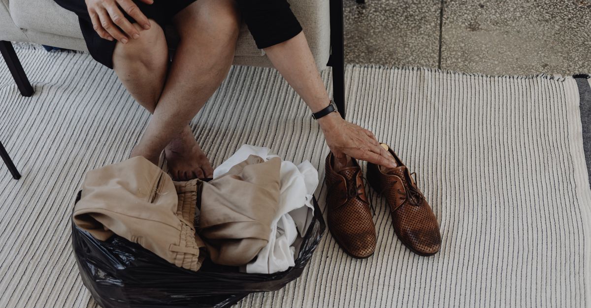 Eine Person sortiert am Boden Kleidungsstücke und Schuhe in eine Tüte zum Aussortieren.