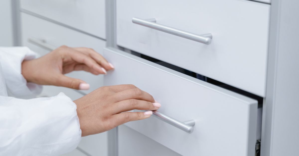 Zwei Hände öffnen eine weiße Auszugsschublade mit Metallgriffen an einem Schrank.