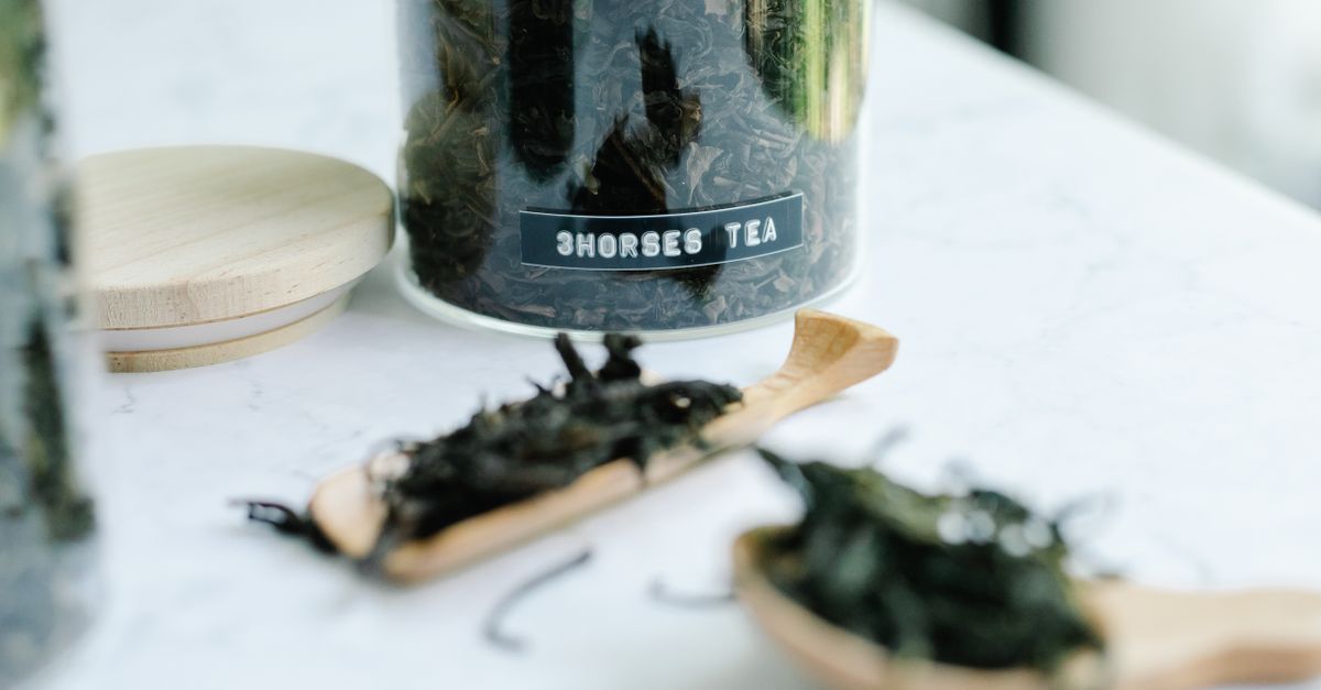 Getrocknete Algenblätter liegen auf Holzlöffeln neben einer offenen Teedose mit Aufschrift 'Horses Tea' auf einer Marmorplatte.