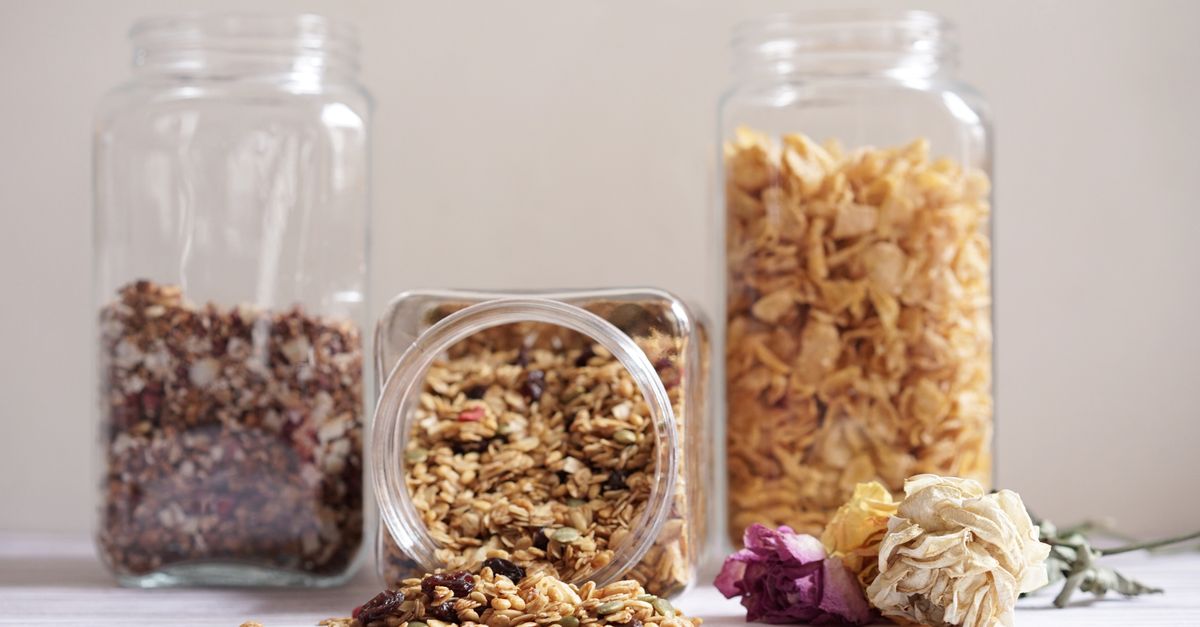 Mehrere durchsichtige Glasbehälter mit Getreideflocken und Müsli stehen offen auf einer hellen Oberfläche.