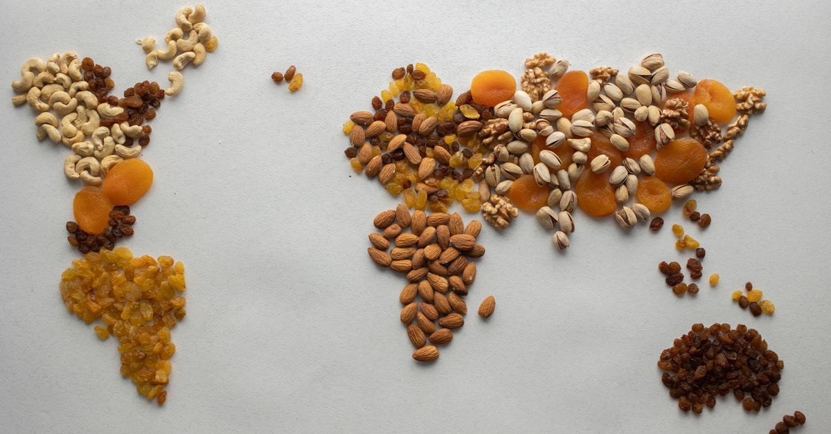 Getrocknete Früchte und Nüsse wie Aprikosen, Rosinen, Cashews und Pistazien zu einer Weltkarte auf einer weißen Fläche angeordnet.