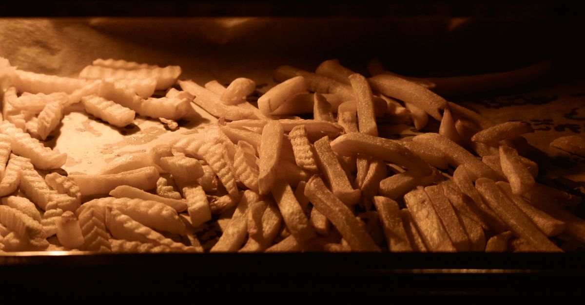 Frittierte oder gebackene Kartoffelstäbchen liegen ausgebreitet auf einem Blech im Ofen.