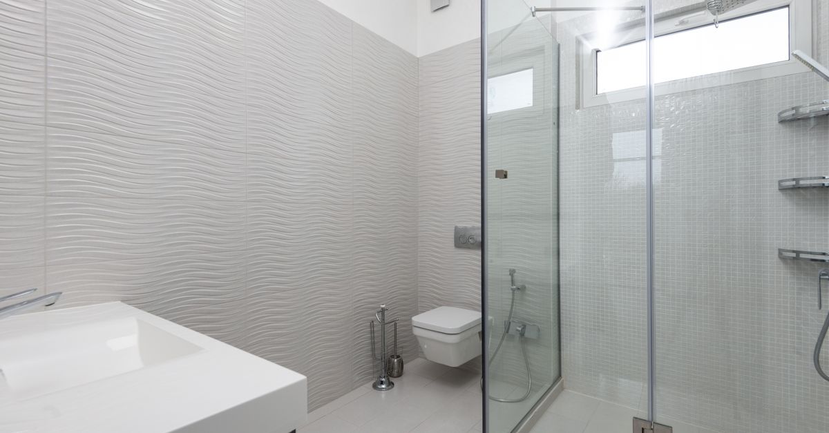 Sauberes, modernes Badezimmer mit gewellten weißen Fliesen und einer blitzsauberen Glasduschkabine.