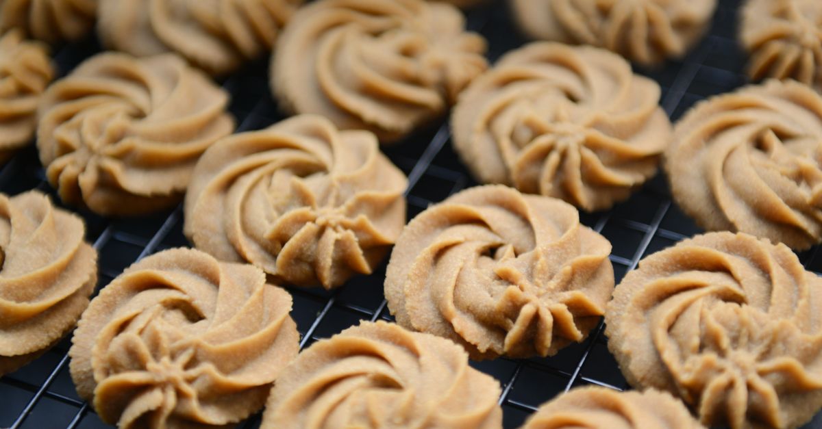 Frisch gebackene, goldbraune Spritzgebäck-Plätzchen liegen in Reihen auf einem schwarzen Kuchengitter zum Abkühlen.
