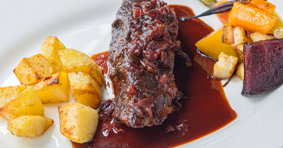 Ein Teller mit geschmortem Fleisch in dunkler Sauce, serviert mit Bratkartoffeln und geröstetem Gemüse.