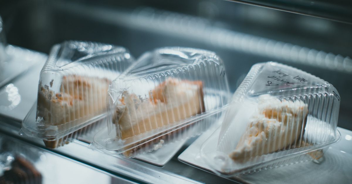 Drei in Plastikschalen verpackte Kuchenstücke liegen in einer Vitrine, eines mit einem handgeschriebenen Etikett.