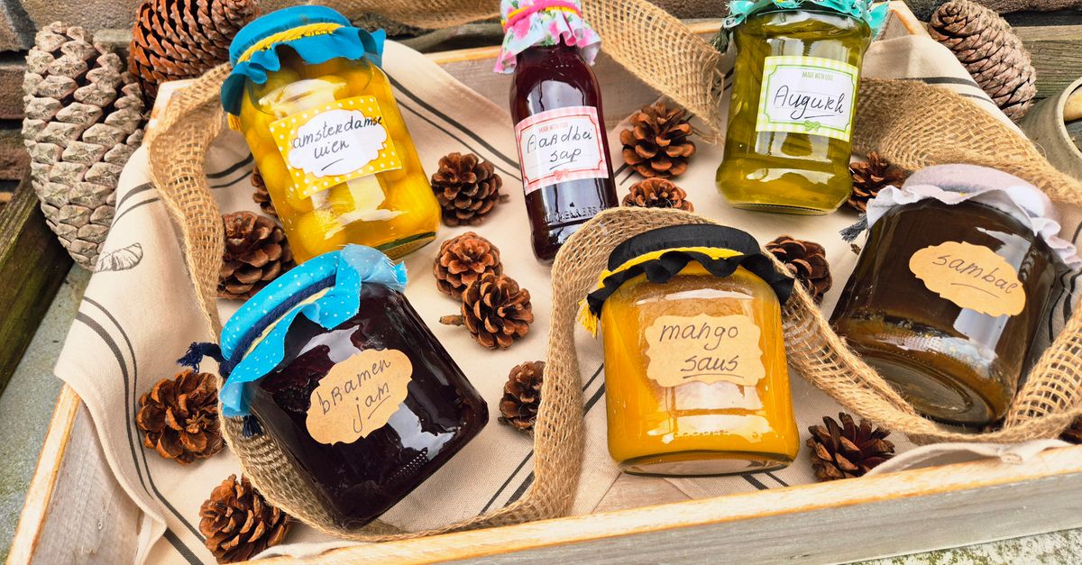 Mehrere selbstgemachte Marmeladen- und Sauciengläser in verschiedenen Farben mit handbeschrifteten Etiketten liegen auf einem Holztablett, umgeben von Tannenzapfen.