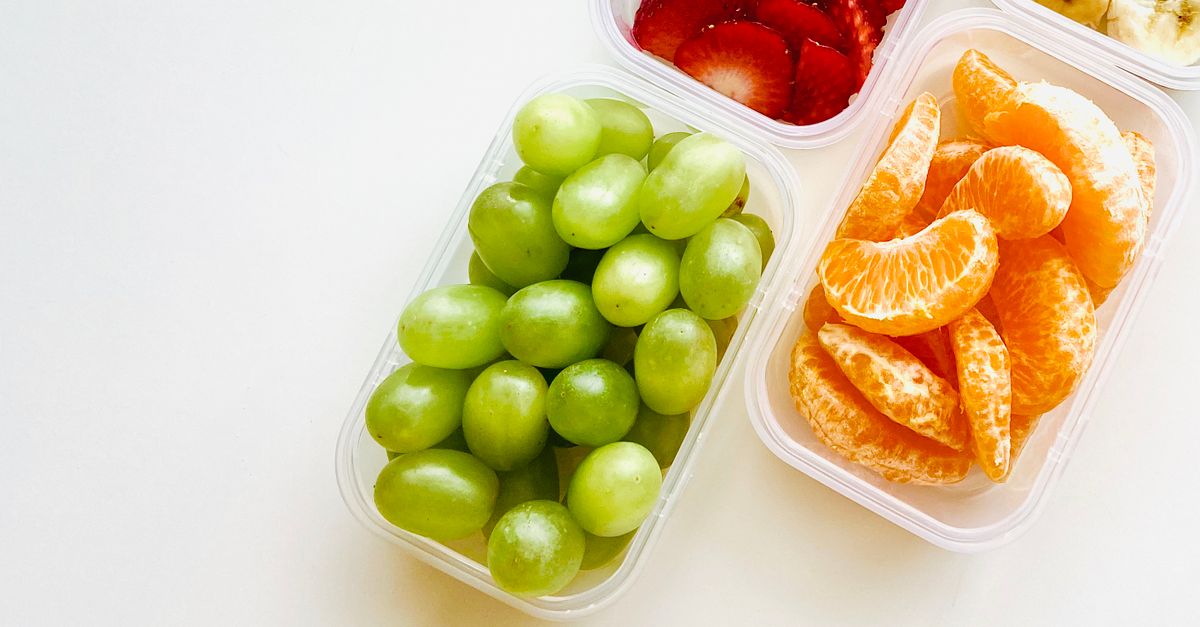 Grüne Weintrauben liegen in einer durchsichtigen Plastik-Vorratsdose neben Behältern mit Erdbeeren und Mandarinenstücken.